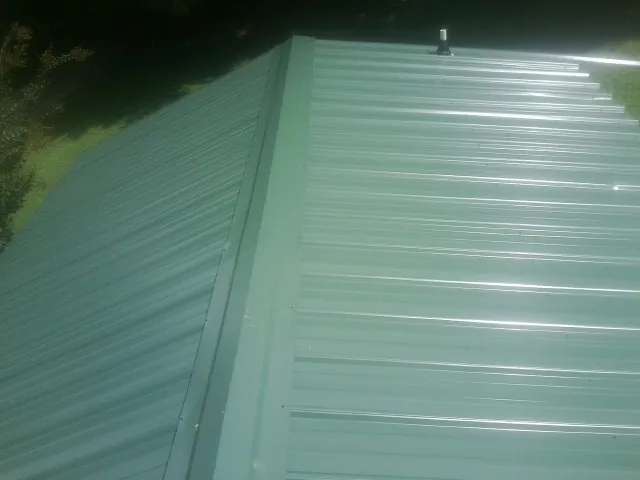 New green metal panels meeting at the ridge of a roof — Flat Roof Repair work by our crew in Immokalee