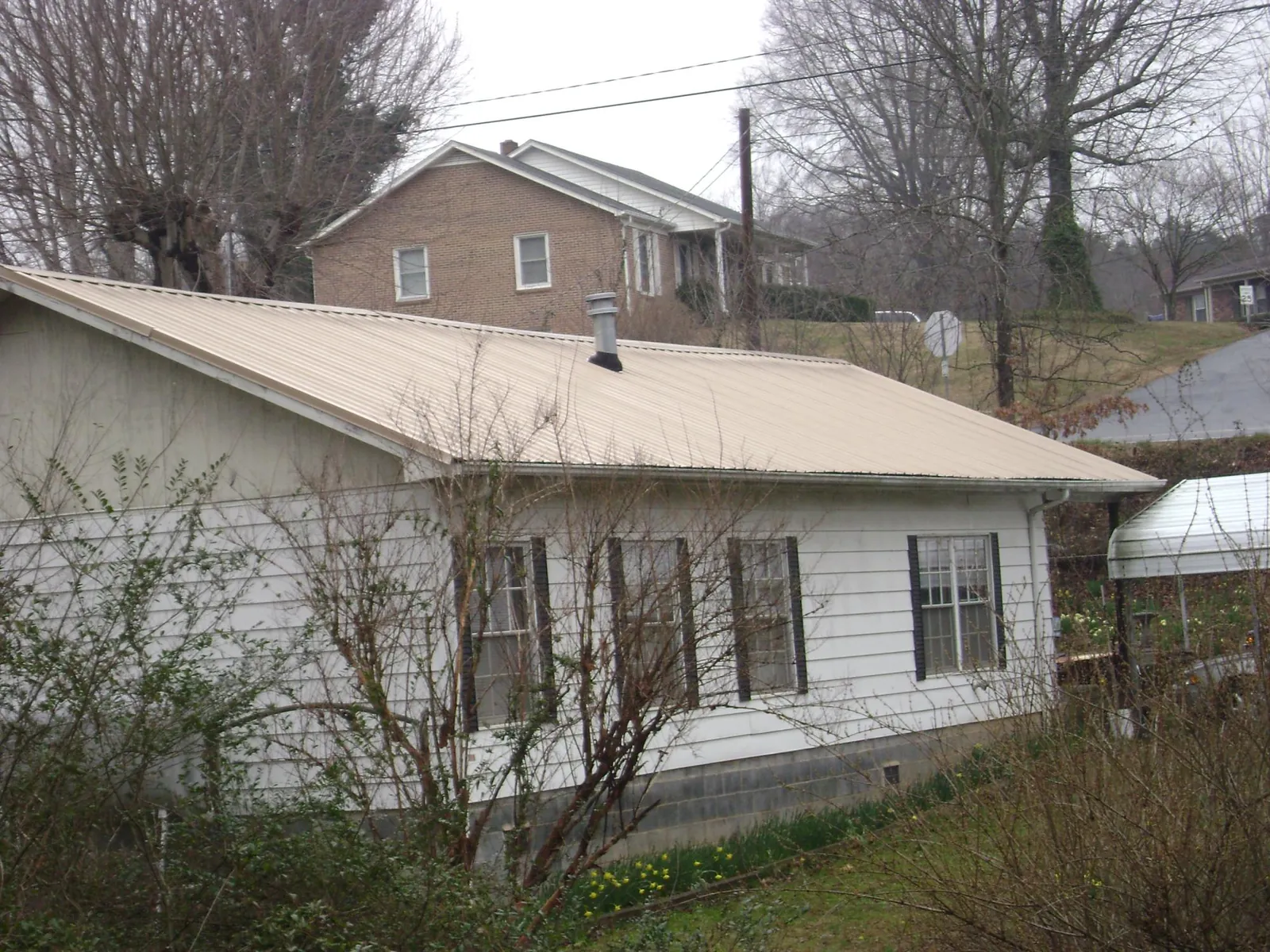 Tan metal roof on a white sided house set into a hillside — Commercial Roofing by Roofing Brothers in Immokalee